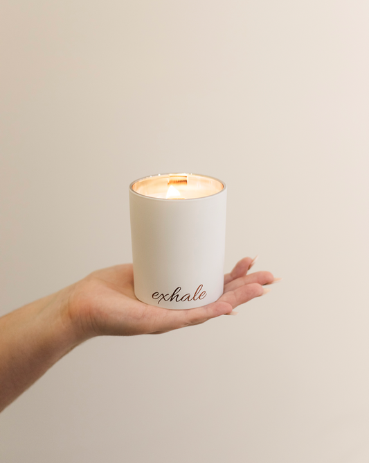 hand holding matte white candle with rose gold exhale word printed and flame lit
